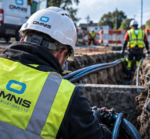 Omnis Communications engineer in hi-vis and hard hat installing fibre ducting in an open trench